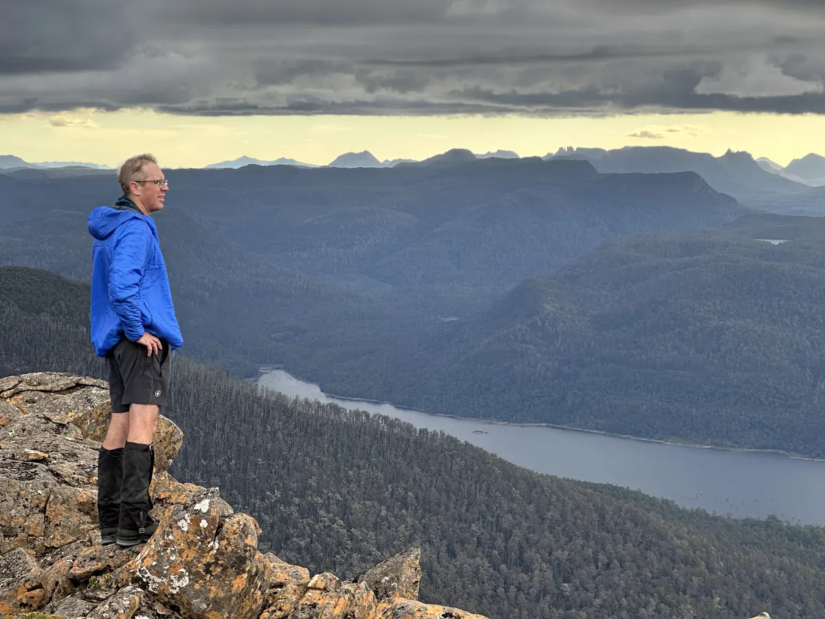 Matthew Will on a summit in the Tasmanian highlands, looking out over a lake and the ranges beyond